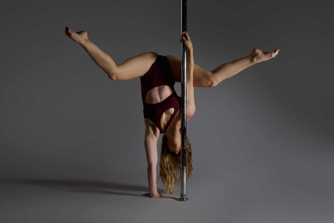Jen Pole Academy doing an Ayesha Handstand on a pole with a grey background